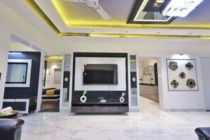 Un salon moderne doté d’un grand téléviseur à écran plat, d’un ventilateur de plafond et d’œuvres d’art décoratives murales.
