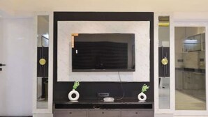 Een moderne woonkamer met een grote flatscreen-televisie aan een zwarte muur, omlijst door twee witte decoratieve vazen en een kleine plant.