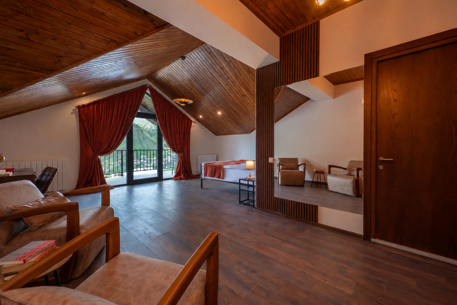 Amplio dormitorio tipo loft con techo inclinado, una ventana grande con cortinas rojas, una cama, un escritorio y una silla.