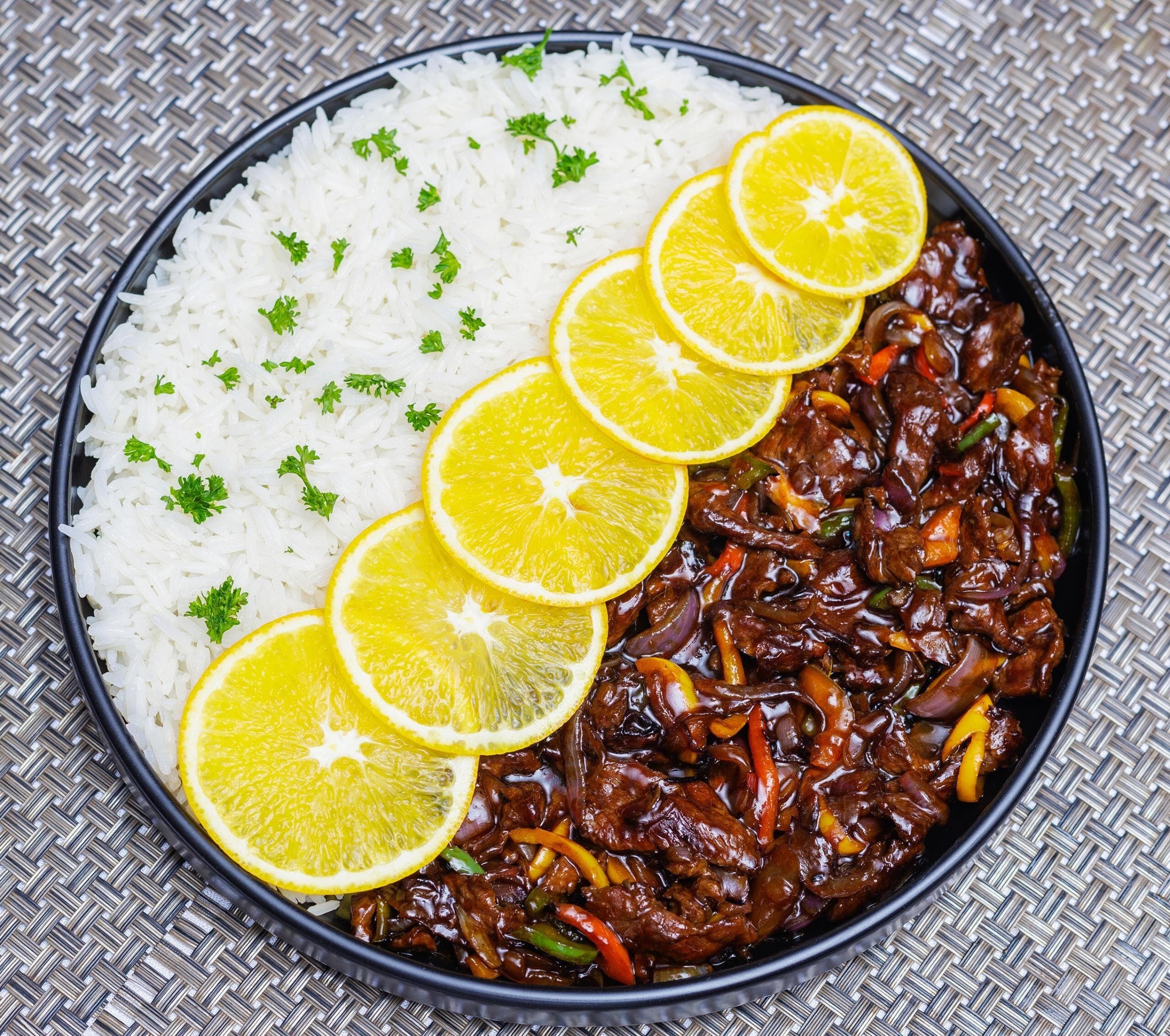 A bowl of white rice garnished with parsley and lemon slices, accompanied by a stir-fry of beef and vegetables.