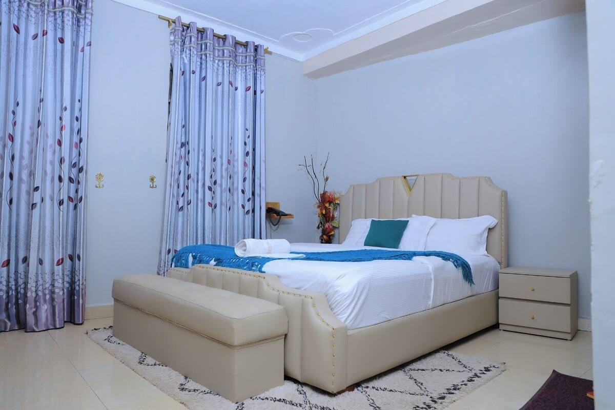A bedroom with a bed, nightstands, a bench, and curtains.