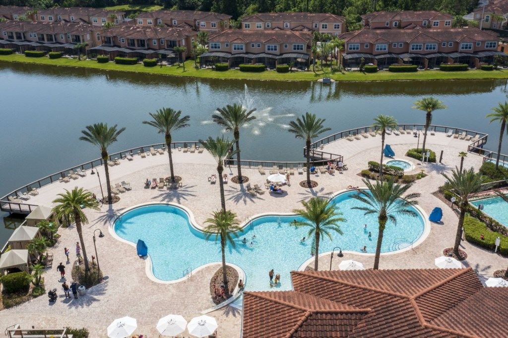 Un resort con una piscina grande, palmeras y vistas a un lago.