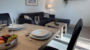 Un coin repas avec une table dressée pour deux personnes, un saladier de fruits et un tableau encadré accroché au mur.
