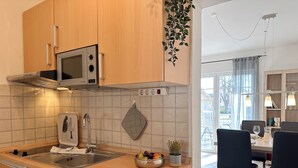 Une cuisine moderne avec des armoires en bois, un évier en acier inoxydable, un four à micro-ondes et un lave-vaisselle. On trouve un saladier rempli de fruits sur le comptoir et une plante suspendue.