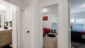 Passadís que condueix a una habitació amb un llit, una finestra amb persianes, una porta i un felpuc.