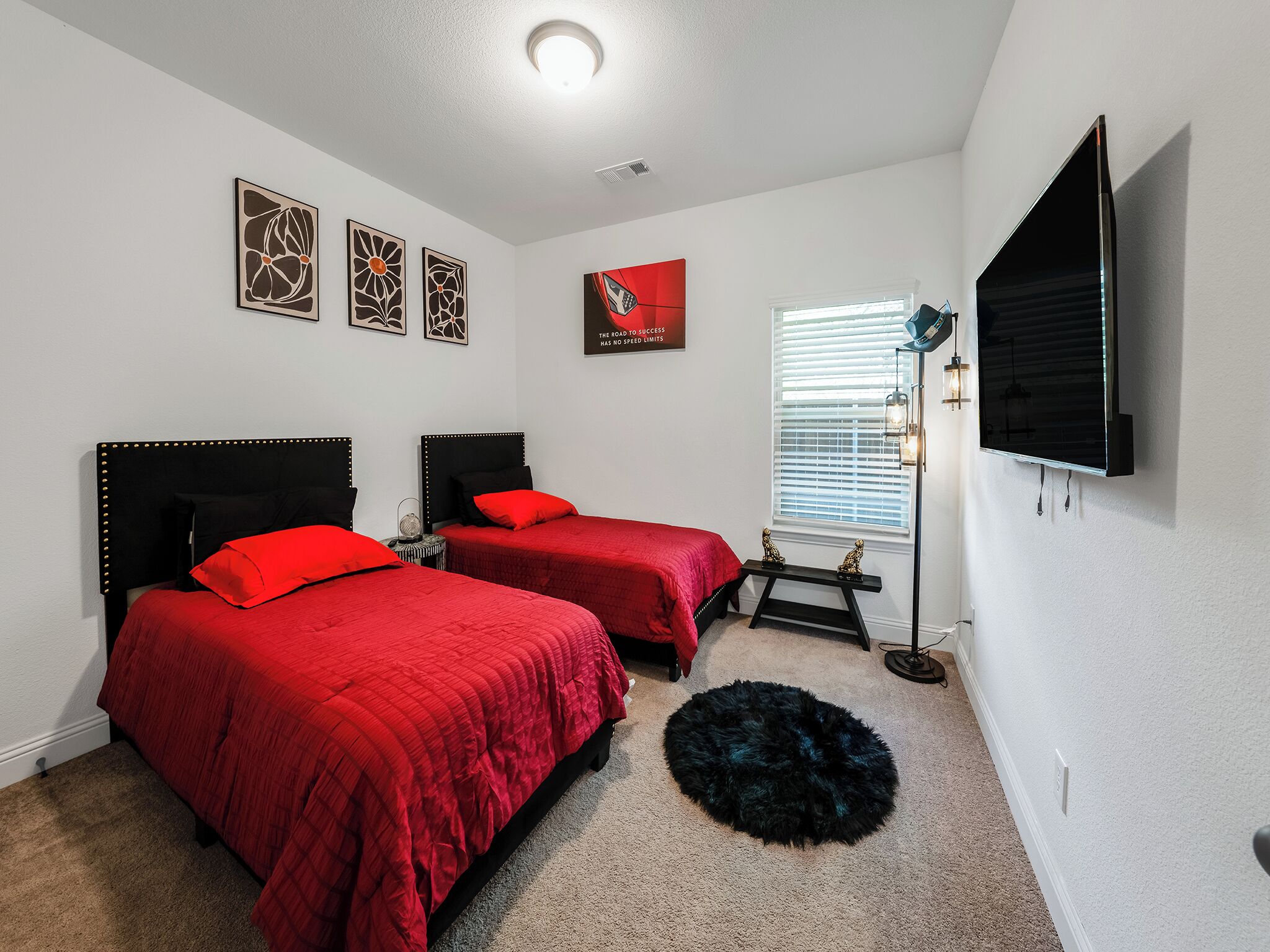 A bedroom with two beds, a TV, artwork, and a window with blinds.