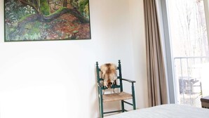Makuuhuone, jossa on sänky, tuoli, taulu ja ikkuna, jossa on verhot.