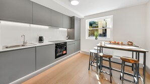 A modern kitchen with grey cabinets, a built-in oven, a sink, and a bar stool area.