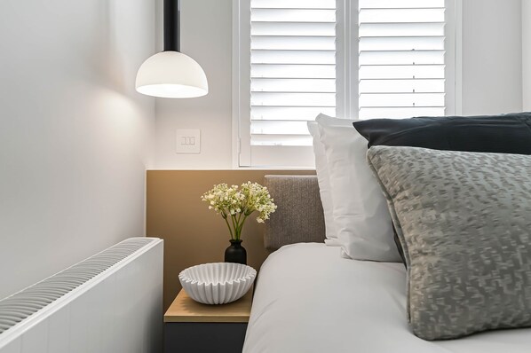 A neatly arranged bedroom with a bed, bedside table, lamp, and a vase with flowers.