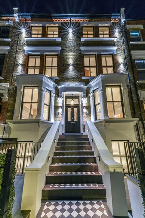 A multi-story building with a central entrance, a staircase leading up to it, and a checkered tile pattern on the steps.