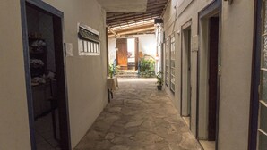 A narrow stone-paved corridor with a wooden ceiling, leading to a wooden door at the end. - Suite Confort 201 (Centro Diamantina)