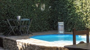 A swimming pool with a stone wall, a metal water fountain, and a table with chairs. - Suite Confort 201 (Centro Diamantina)