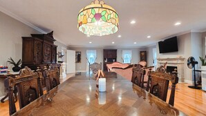 A spacious living room with a large wooden dining table, a chandelier, and a fireplace. - Spacious Waterview Home - Spa, Pool Table & Fireplaces – for Families & Reunion (Bourne)