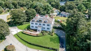 A large, single-story house with a symmetrical facade, surrounded by lush greenery and a winding road. - Spacious Waterview Home - Spa, Pool Table & Fireplaces – for Families & Reunion (Bourne)