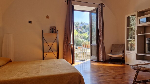 A bedroom with a bed, a chair, a shelf, and a balcony with curtains. - Apartment Sorrento "in Corso Italia" (Sorrento)