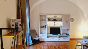 A living room with a TV, shelves, a clock, and a sofa. - Apartment Sorrento "in Corso Italia" (Sorrento)