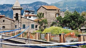 A stone church with a bell tower, surrounded by residential buildings and greenery, with mountains in the background. - Apartment Sorrento "in Corso Italia" (Sorrento)