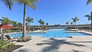Piscina con sillas de descanso y palmeras, bajo un cielo azul despejado.