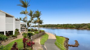 A waterfront hotel with a paved walkway, palm trees, and a view of the water.