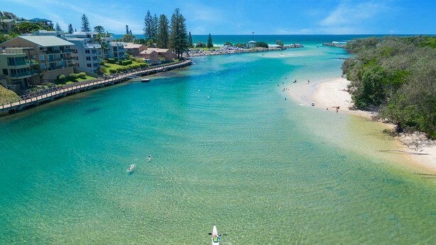 A coastal resort with clear turquoise waters, a sandy beach, and a bridge connecting to a building complex.