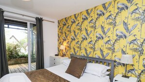 Ein Schlafzimmer mit einem Bett, einem Nachttisch, einer Lampe und Blick ins Freie.