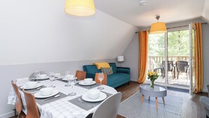 Ein Essbereich mit Tisch für vier Personen, einer Couch und einem Balkon mit Stühlen.
