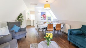 Ein modernes Wohnzimmer mit Essbereich, ausgestattet mit einer Couch, einem Couchtisch mit Blumenvase und einem Esstisch, gedeckt für vier Personen.