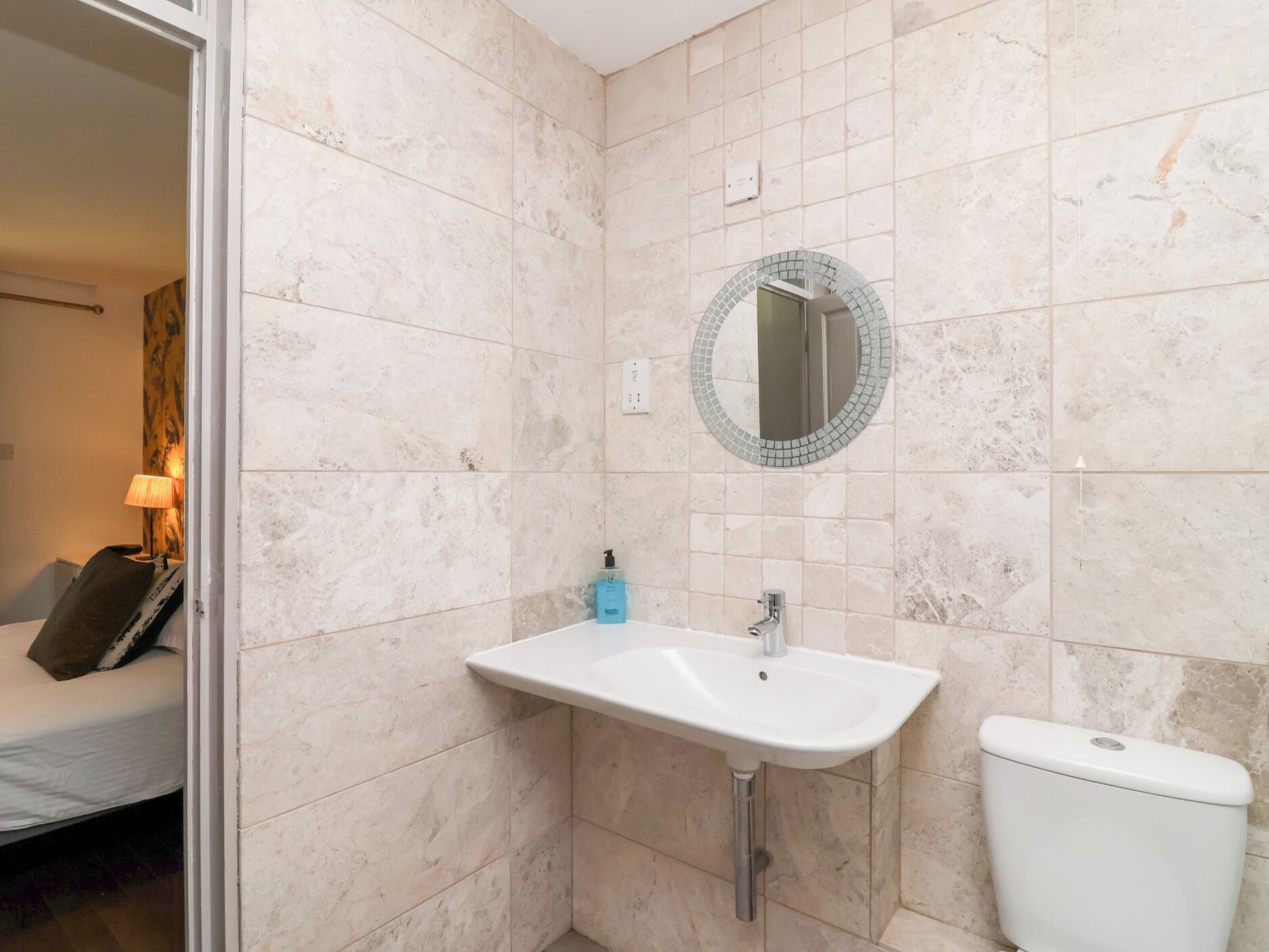 A bathroom with a white sink, a toilet, and a mirror with a mosaic border.