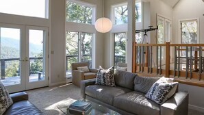 A spacious living room with large windows, a leather sofa, a glass coffee table, and a view of the outdoors. - Cliffs Edge-A Contemporary Mountain Home (Wintergreen Resort)