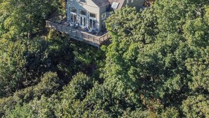 A house surrounded by dense forest, with a prominent roof and a visible deck area. - Cliffs Edge-A Contemporary Mountain Home (Wintergreen Resort)