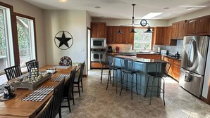 Une cuisine moderne avec des meubles en bois, un réfrigérateur en acier inoxydable et un coin repas comprenant une grande table et des chaises.