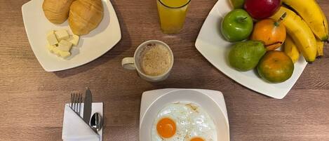 Una escena de desayuno con croissants, fruta, huevos y una taza de café sobre una mesa de madera.
