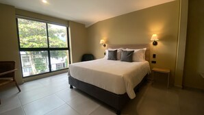 Un dormitorio moderno con una cama grande, dos lámparas de noche, vistas amplias por un ventanal y una pequeña zona de estar.