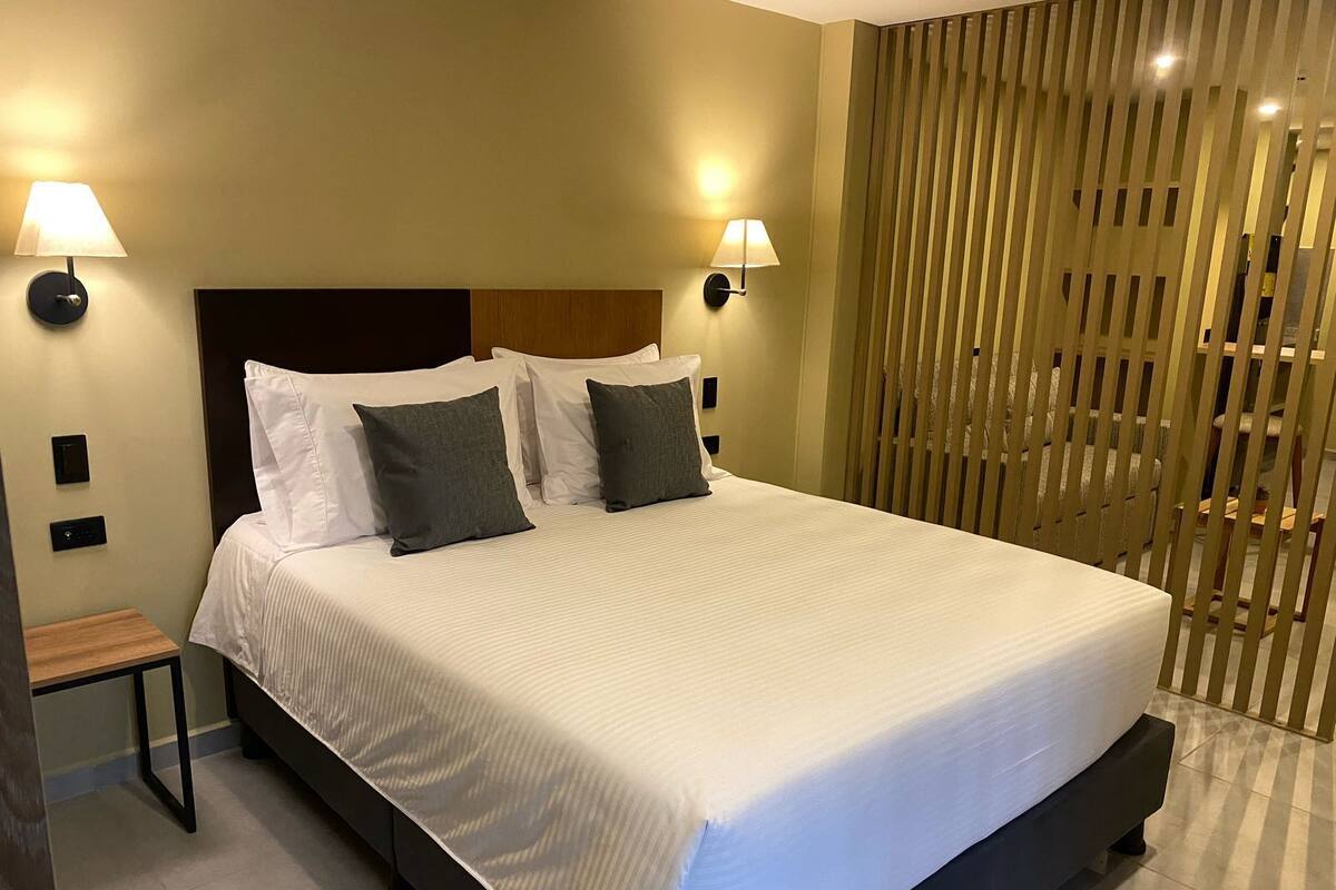 A modern hotel room with a large bed, two bedside lamps, and a wooden headboard.