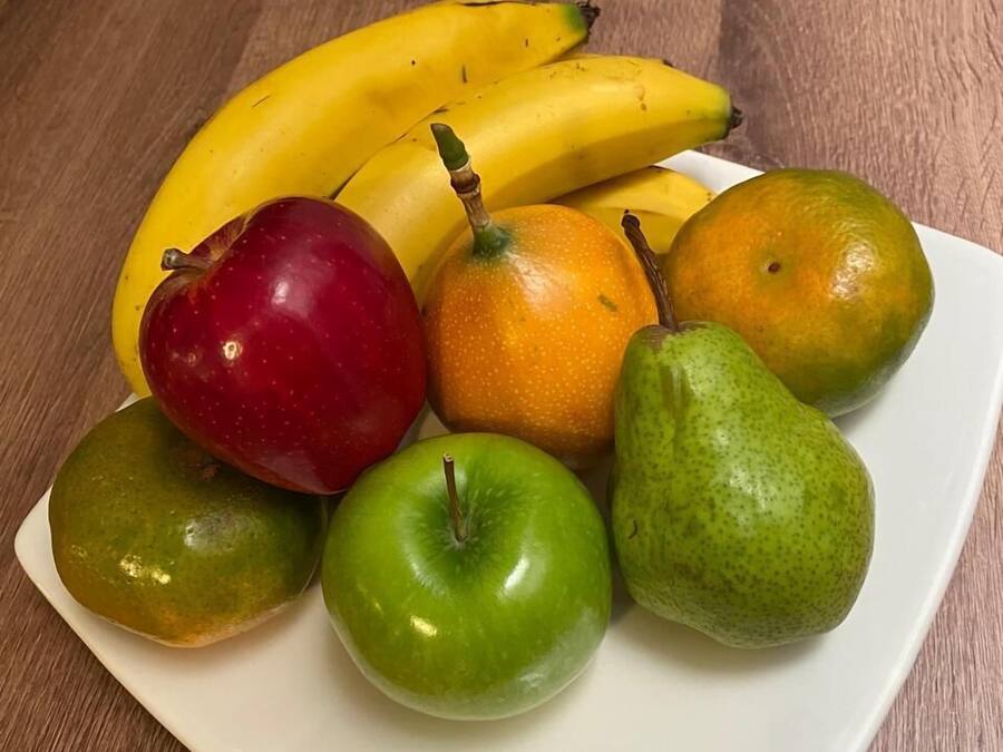 En tallrik med olika frukter, inklusive bananer, äpplen och päron, står på ett träbord.