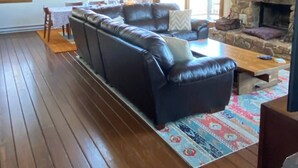 A spacious living room with a large leather sectional sofa, a wooden coffee table, and a stone fireplace. - Slopes @ Tyro (Wintergreen Resort)