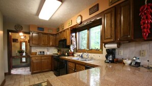 A kitchen with wooden cabinets, a granite countertop, a sink, a stove, and a window with a view of greenery. - Slopes @ Tyro (Wintergreen Resort)