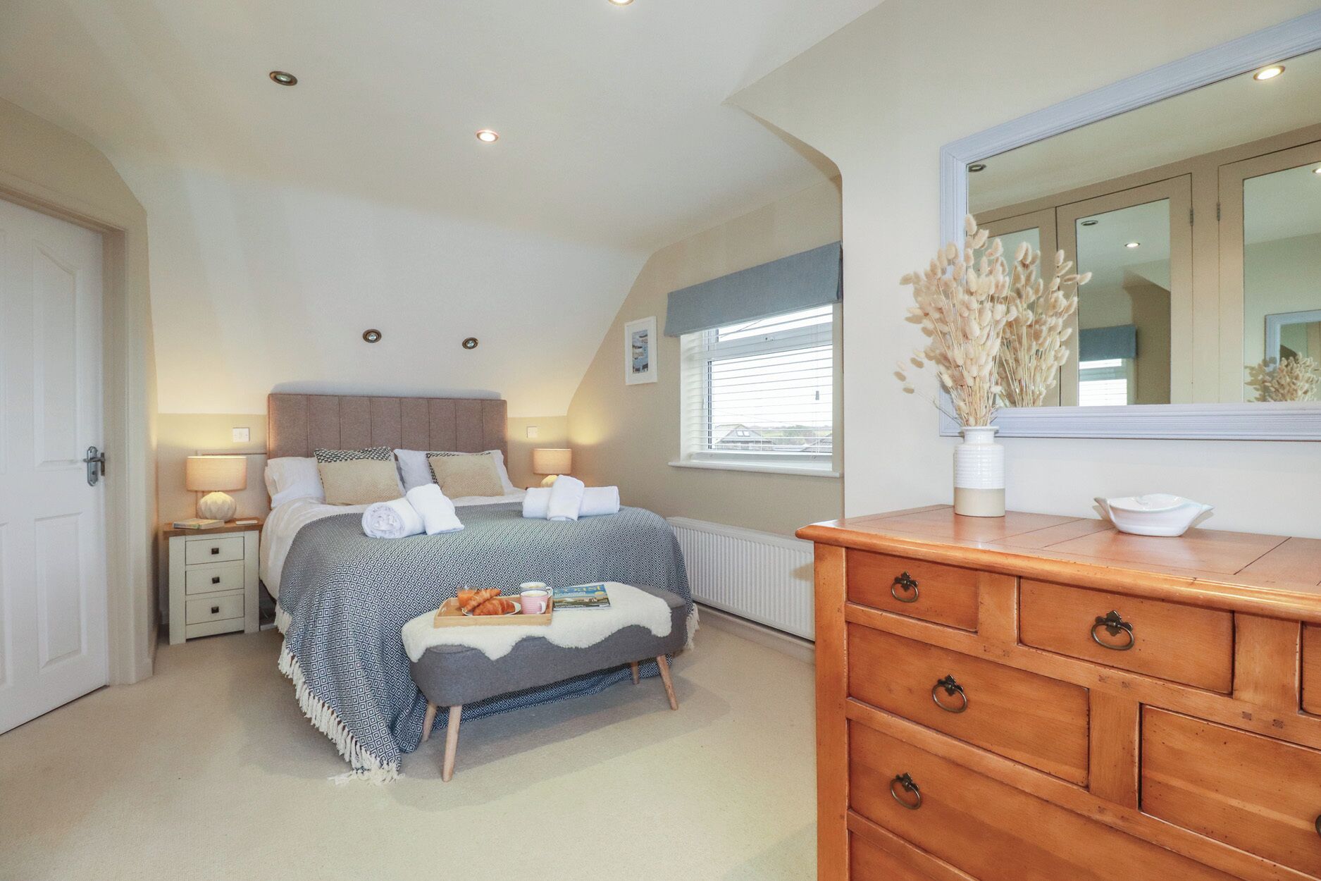 A bedroom with a bed, bedside tables, a dresser, a window with blinds, a radiator, and a mirror.