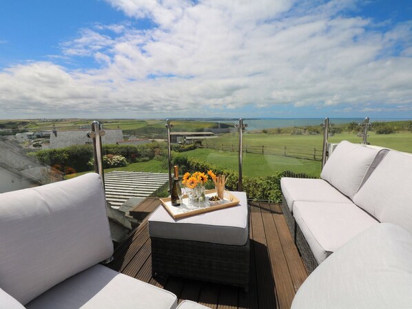 Une terrasse avec un canapé blanc, une petite table sur laquelle se trouvent une bouteille et des verres, et une vue sur un terrain de golf et des champs.