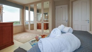 A bedroom with a large bed, a wardrobe, a desk, and a window with a view. - Coastman's Nest (Newquay)