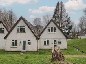 A row of two-story houses with white walls and brown roofs, set in a grassy area with trees in the background. - Valley Lodge 38 (Gunnislake)