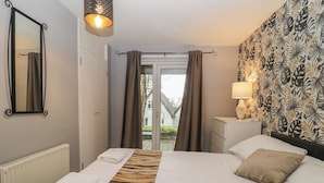 A hotel room with a bed, a nightstand, a lamp, a window with curtains, and a view of the outside. - Valley Lodge 38 (Gunnislake)