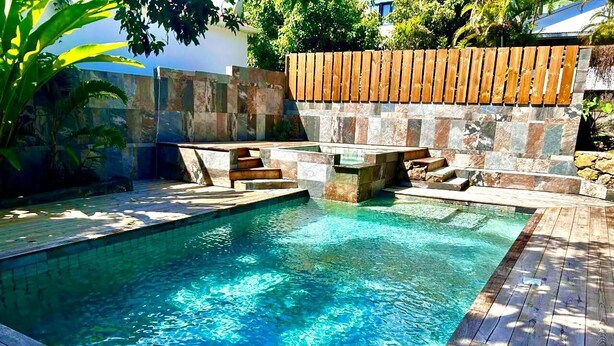 A swimming pool with clear blue water, surrounded by a wooden deck and stone walls. - Les Longanis Sea View and Shared Pool Mont Vert (Mont Vert les Bas)