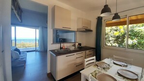 A modern kitchen with a large window, a dining area with a table set for two, and a balcony with a view. - Les Longanis Sea View and Shared Pool Mont Vert (Mont Vert les Bas)