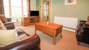 Un salon avec une table basse en bois, des canapés en cuir, un téléviseur posé sur un meuble en bois et un radiateur.