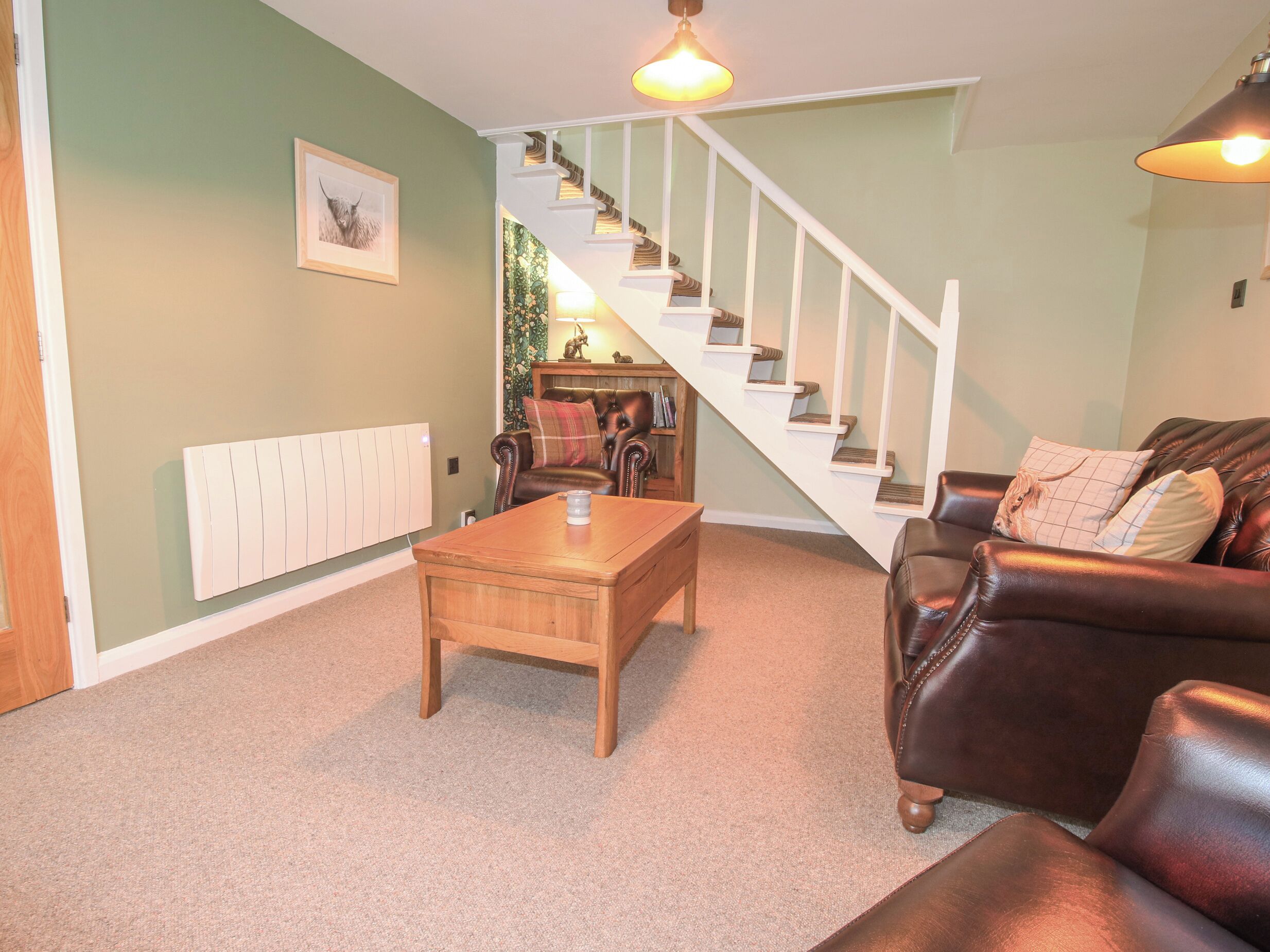 A living room with a staircase, a brown leather sofa, a wooden coffee table, and a framed picture on the wall.