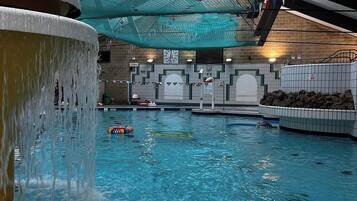 Ein Hallenbad mit Wasserfall, einer Uhr und einer Fliesenwand mit geometrischem Muster.