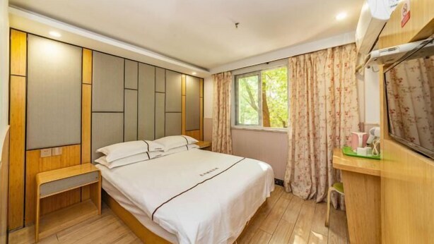 A bedroom with a bed, bedside table, window with curtains, and a small desk with a chair. - Wen Feng Hotel (Shanghai)
