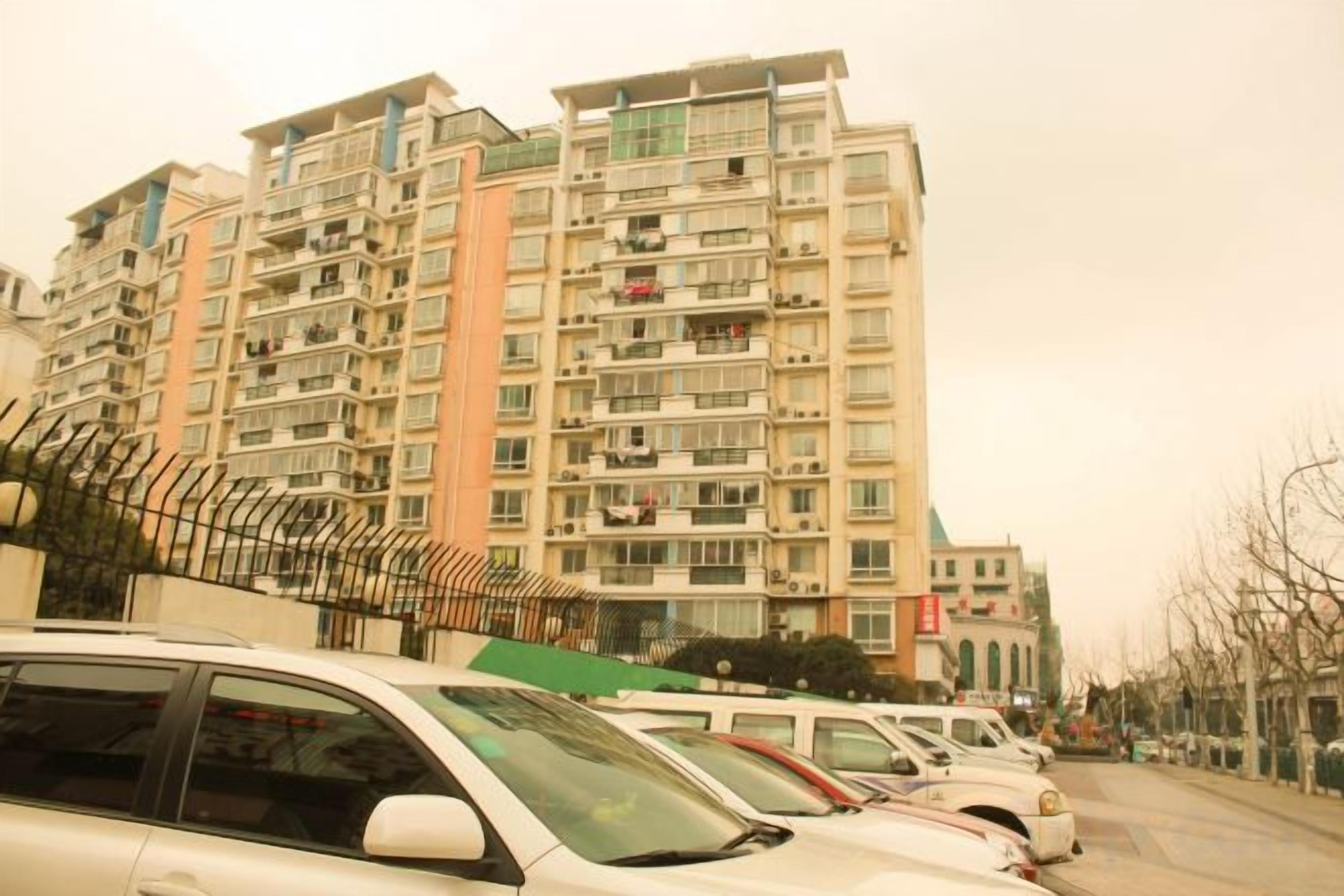 Un edificio residenziale a più piani con balconi, auto parcheggiate e cielo sereno.