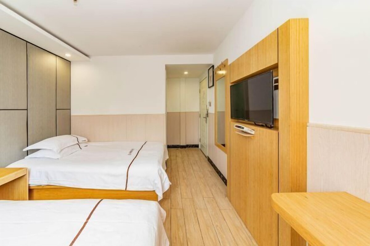 A hotel room with two beds, a wooden desk, a TV mounted on the wall, and a mirror.